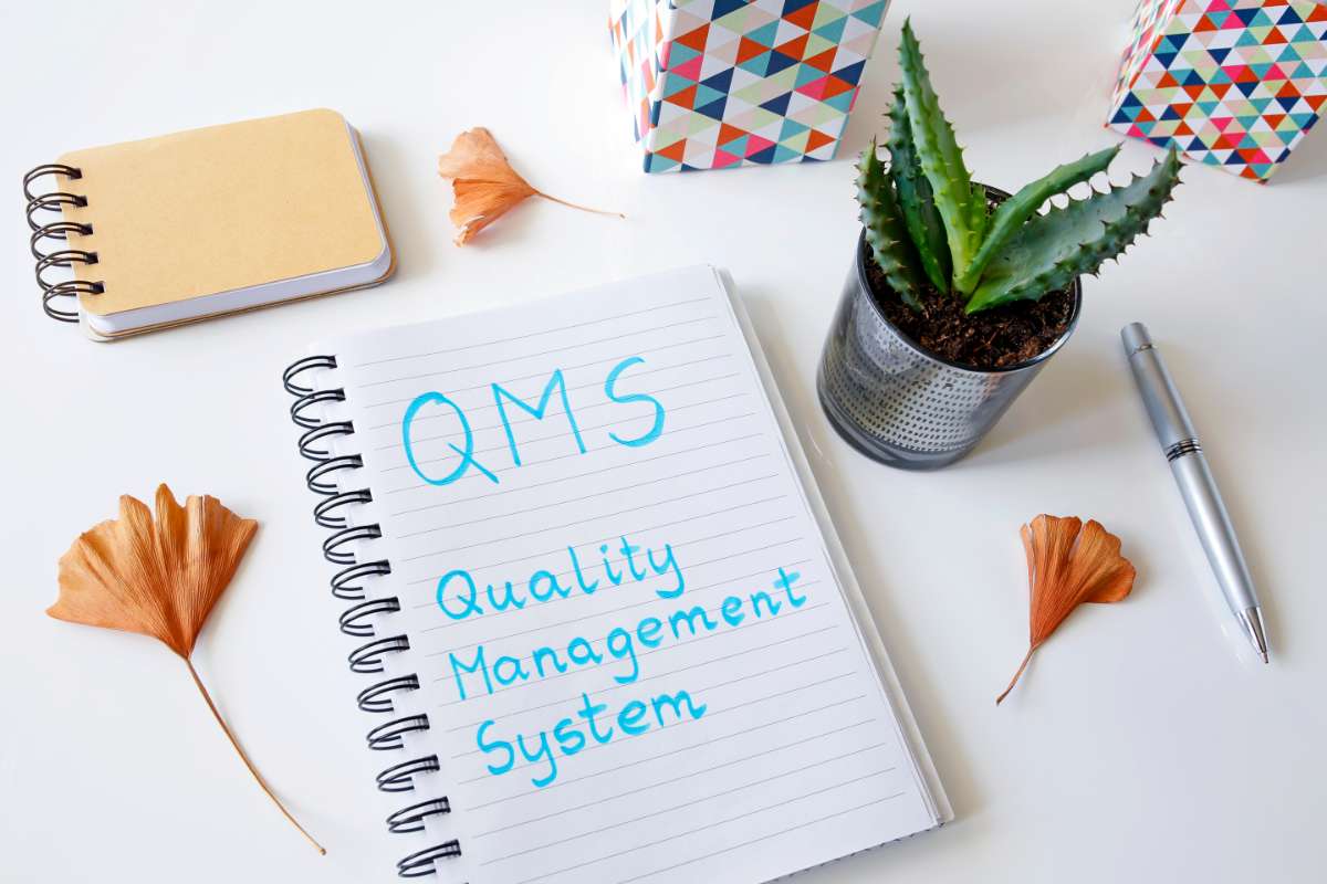 Cahier de notes ouvert avec écrit au fluo bleu Quality Management System (QMS)