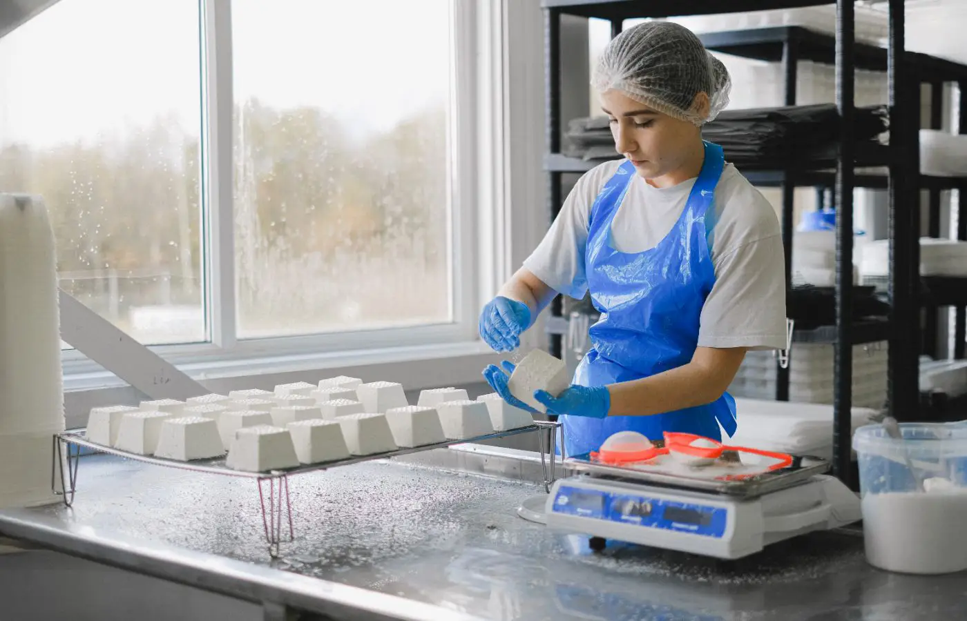 Travailleuse en tenue hygiénique manipulant des produits alimentaires sur une ligne de production, symbolisant le respect des normes de sécurité et de qualité agroalimentaires.